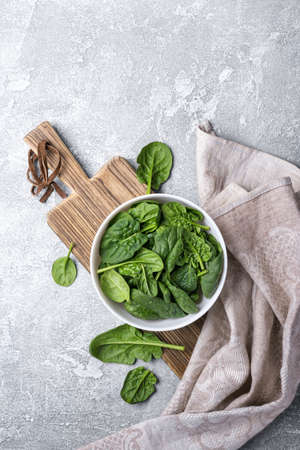 Top view of bowl with green fresh baby spinach on wooden board and grey concrete background