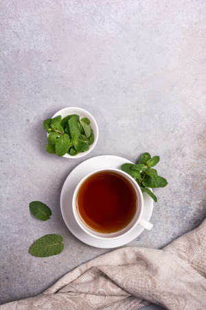 Top view of white cup with fragrant tea and green fresh mint leaves on gray concrete backgroundの写真素材