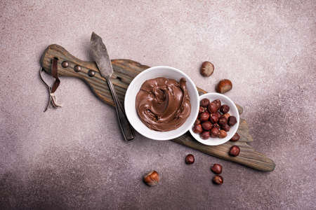 Delicious chocolate cream or brown nut butter, paste and whole hazelnut as ingredient for tasty homemade dessert on concrete backgroundの写真素材