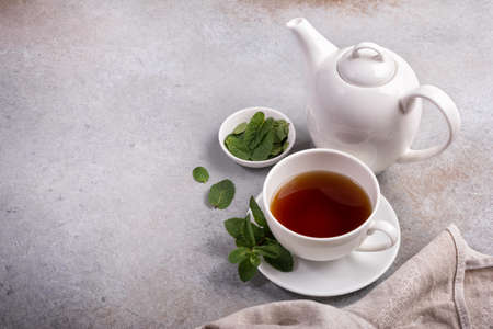 White cup of fragrant tea with kettle and green fresh mint leaves on gray concrete backgroundの写真素材