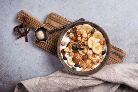 Top view of granola with yogurt, fresh banana, almonds and hazelnuts, pumpkin seeds for healthy...