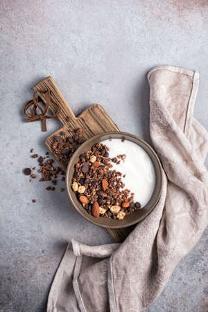 Top view of granola with yogurt, chocolate drops and almond nuts for healthy breakfast on grey concrete backgroundの写真素材