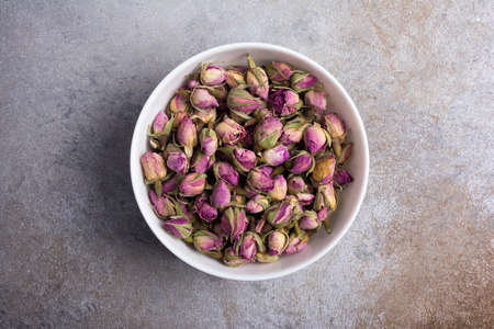 Top view of white bowl with dried rose buds for fragrant tea on grey concrete backgroundの写真素材