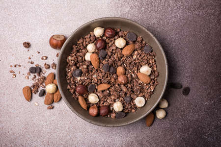 Top view of granola with dark chocolate deops, almond and hazelnut in bowl for nutritious breakfast on brown concrete backgroundの写真素材