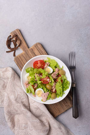 Top view of healthy and tasty salad with tuna fish, fresh lettuce, cherry tomatoes, quail egg and green olives on grey concrete backgroundの写真素材