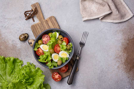 Top view of healthy and tasty salad with fresh lettuce, cherry tomatoes, quail egg and green olives on grey concrete backgroundの写真素材