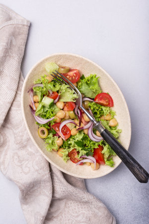 Healthy and tasty vegan food. Top view of chickpea salad with lettuce, cherry tomatoes, onion, cucumber and green olives on grey concrete backgroundの写真素材