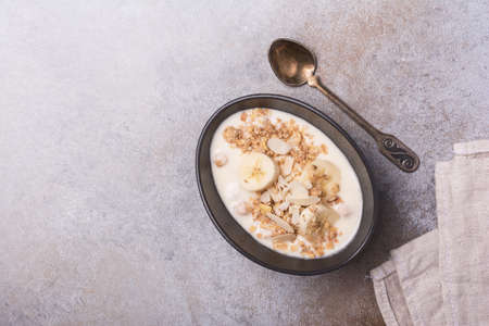 Top view of granola with yogurt, fresh banana and almond nuts for healthy breakfast on grey concrete backgroundの写真素材