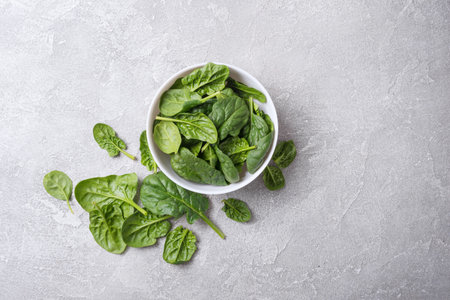 Top view of bowl with green fresh baby spinach on grey concrete background