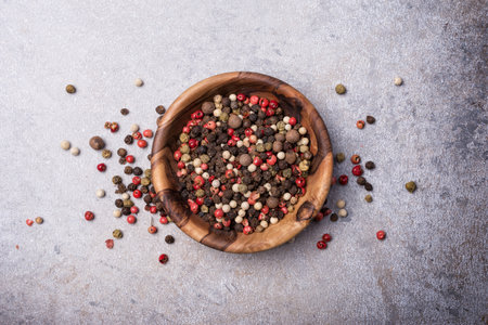 Top view of mix peppercorns in wooden bowl for spicy and aromatic food on grey concrete backgroundの写真素材