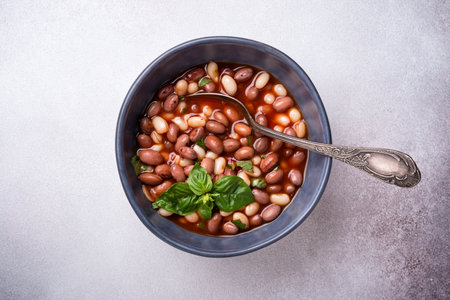 Top view of spicy dish with beans in tomato sauce with fresh basil on grey concrete backgroundの写真素材