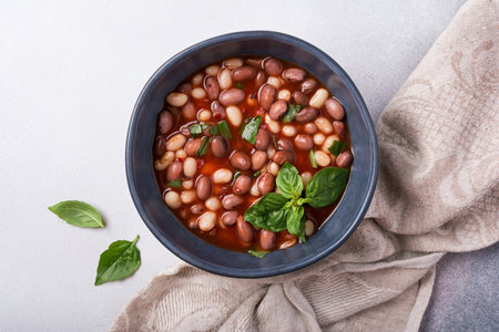 Top view of spicy dish with beans in tomato sauce with fresh basil on grey concrete backgroundの写真素材