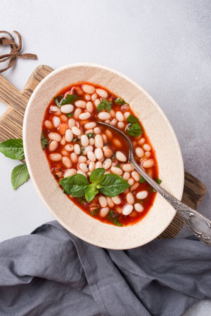 Top view of spicy dish with beans in tomato sauce with fresh basil on grey concrete backgroundの写真素材
