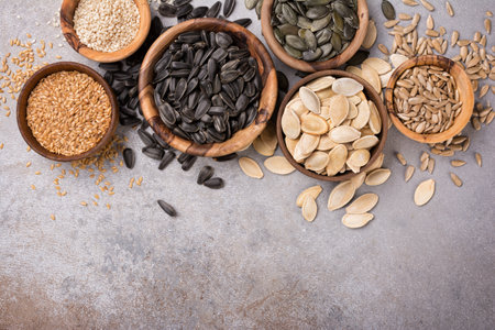 Top view of wooden bowls with pumpkin, sunflower, flax and sesame seeds for healthy nutrition on grey concrete backgroundの写真素材