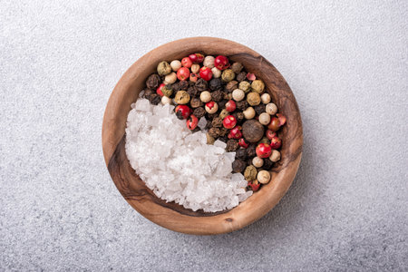 Top view of mix peppercorns and sea salt in wooden bowl for spicy and aromatic food on grey concrete backgroundの写真素材