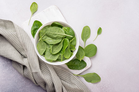 Top view of bowl with green fresh baby spinach on wooden board and grey concrete backgroundの写真素材