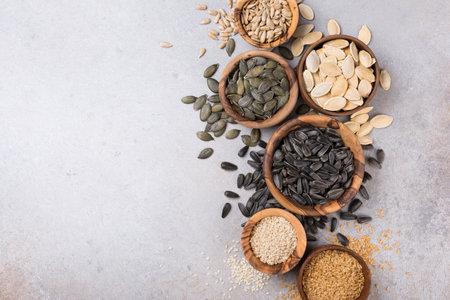 Top view of wooden bowls with pumpkin, sunflower, flax and sesame seeds for healthy nutrition on grey concrete background with copy spaceの写真素材