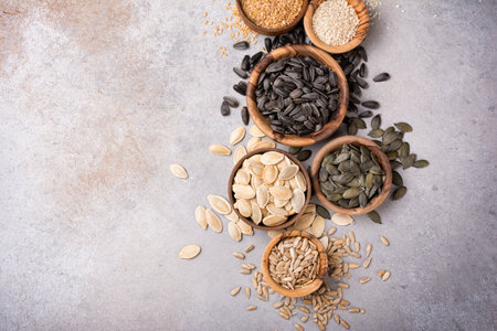 Top view of wooden bowls with pumpkin, sunflower, flax and sesame seeds for healthy nutrition on grey concrete background with copy spaceの写真素材