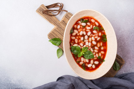 Top view of spicy dish with beans in tomato sauce with fresh basil on grey concrete backgroundの写真素材