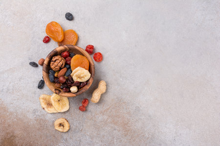 Top view of wooden bowl with dried fruit, berries and nuts as ingredient for tasty and healthy meal on grey concrete background with copy spaceの写真素材