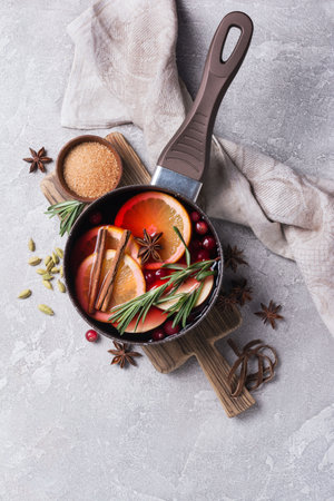 Flat lay of autumn or winter traditional drink with oranges, cranberry, cinnamon, rosemary and other ingredients on grey concrete backgroundの写真素材