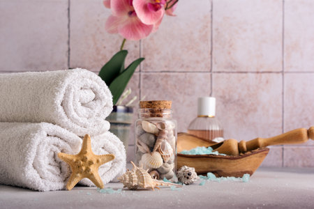 Blue sea salt in wooden bowl with shells, orchid flower and white towels for relax, bath, spa on tile backgroundの写真素材