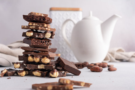 Pieces of broken tasty milk, dark and air chocolate bars with hazelnut  and kettle for tea time, on kitchen backgroundの写真素材