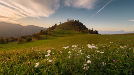 Beautiful morning landscape of church in Slovenia on green hill with blue sky and mountains backgroundの写真素材