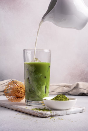 Homemade green matcha tea or latte with ice and milk or cream in trendy glass with bamboo whisk on grey concrete backgroundの写真素材