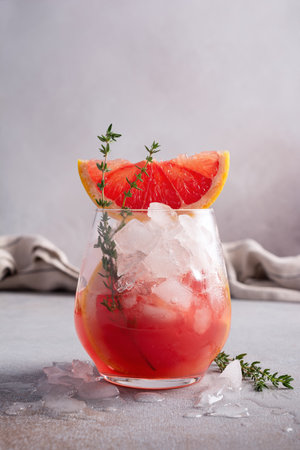 Homemade ice citrus fruit cocktail or mocktail with grapefruit slice in glass for tasty and refreshing break on grey kitchen backgroundの写真素材