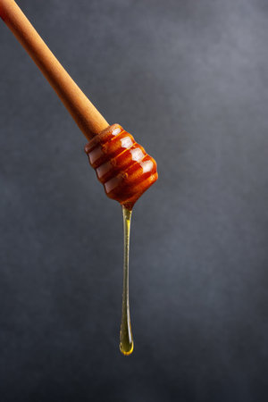 Healthy organic honey pouring with a wooden dipper on dark backgroundの写真素材