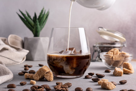 Homemade ice latte. Black coffee with ice and milk or cream in glass for tasty and refreshing break on grey kitchen backgroundの写真素材