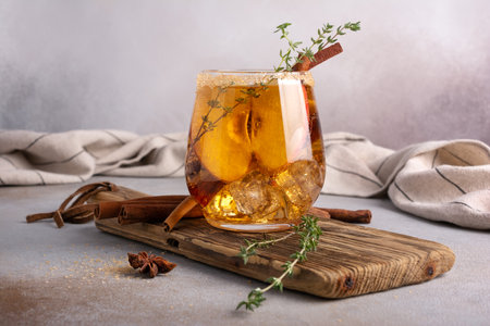 Homemade ice sweet apple cider, cocktail or mocktail with cinnamon, thyme and anise in glass for tasty and refreshing break on grey kitchen backgroundの写真素材