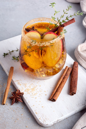 Homemade ice sweet apple cider, cocktail or mocktail with cinnamon, thyme and anise in glass for tasty and refreshing break on grey kitchen backgroundの写真素材