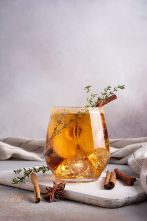 Homemade ice sweet apple cider, cocktail or mocktail with cinnamon, thyme and anise in glass for tasty and refreshing break on grey kitchen backgroundの写真素材