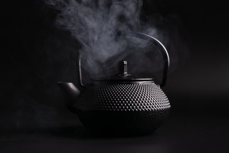 Traditional black asian cast iron hot teapot or kettle with steam on dark backgroundの写真素材