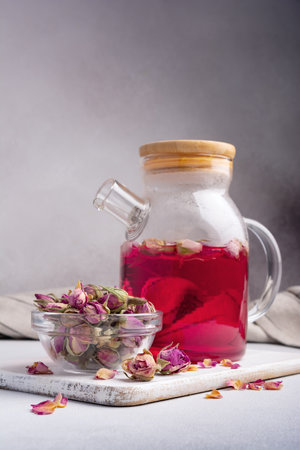 Beautiful flower pink tea in glass teapot with dry rose buds in bowl on grey kitchen backgroundの写真素材