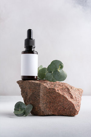 Mockup of skincare cosmetic product. Brown bottle of eco or natural lotion or serum on stone pedestal with eucalyptus branch on grey backgroundの写真素材