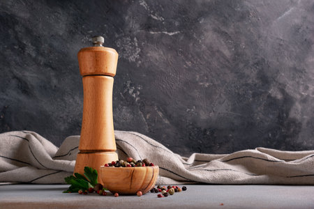 Mix of peppercorns in bowl with wooden pepper mill and green parsley leaves for aromatic food on grey concrete backgroundの写真素材