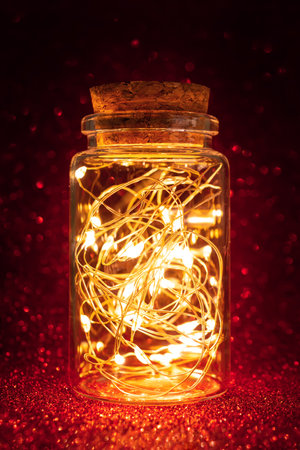 Beautiful lantern with magic lighted garland in glass jar on red shiny glittering backgroundの写真素材