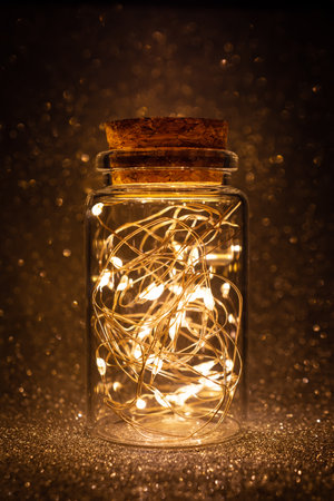 Beautiful lantern with magic lighted garland in glass jar on golden shiny glittering backgroundの写真素材