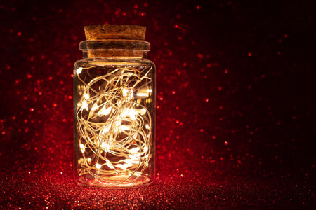 Beautiful lantern with magic lighted garland in glass jar on red shiny glittering backgroundの写真素材
