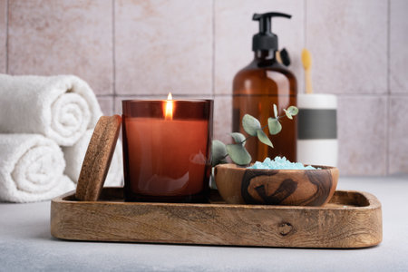 Eco friendly bathroom concept. Sea salt in wooden bowl, toothbrushes in glass, bottle of shower gel and candle for relax and spa on tile backgroundの写真素材
