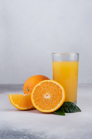 Fresh orange juice in glass with ripe orange fruits on grey backgroundの写真素材