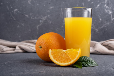 Tasty fresh orange juice in glass with sliced orange and leaves on dark grey concrete backgroundの写真素材