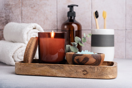Eco friendly bathroom concept. Sea salt in wooden bowl, toothbrushes in glass, bottle of shower gel and candle for relax and spa on tile backgroundの写真素材