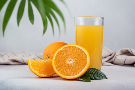 Tasty fresh orange juice in glass with sliced orange and leaves on grey concrete backgroundの写真素材