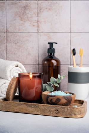 Eco friendly bathroom concept. Sea salt in wooden bowl, toothbrushes in glass, bottle of shower gel and candle for relax and spa on tile backgroundの写真素材