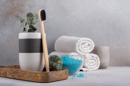 Eco friendly bathroom concept, sustainable lifestyle. Bamboo toothbrush in a glass with white towels, eucalyptus on wooden tray and blue sea saltの写真素材