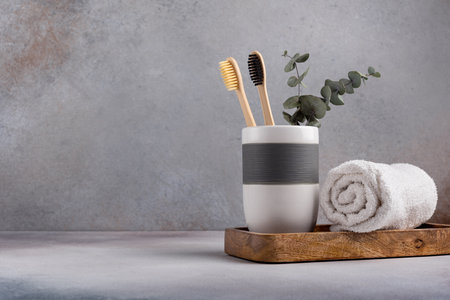 Eco friendly bathroom concept, sustainable lifestyle. Couple of bamboo toothbrush in a glass with white towel and eucalyptus on wooden trayの写真素材